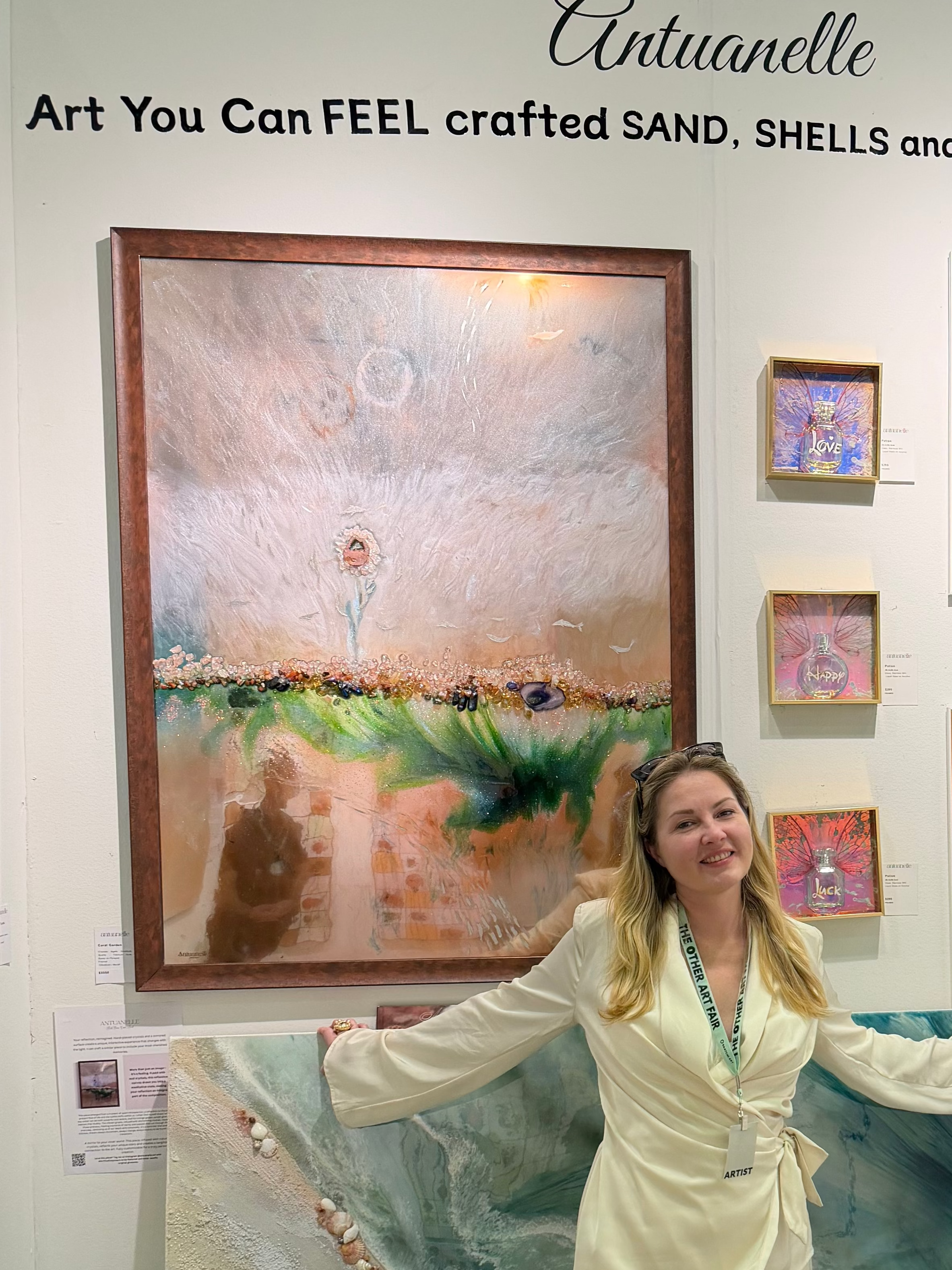 Woman standing in front of art pieces at an exhibition with 'Antuanelle' branding.